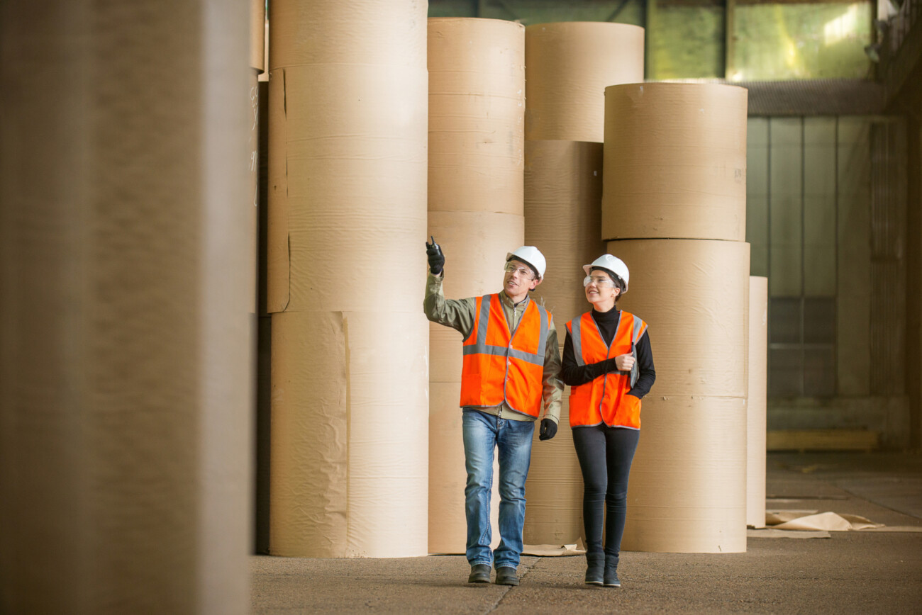 two people in high vis clothing walking through a papermaking facility paper industry