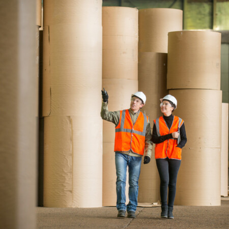 two people in high vis clothing walking through a papermaking facility paper industry