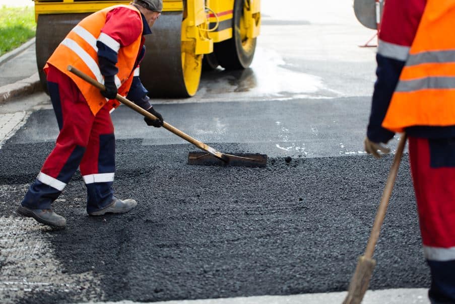 workers dressed in orange PPE laying asphalt roads and paving.